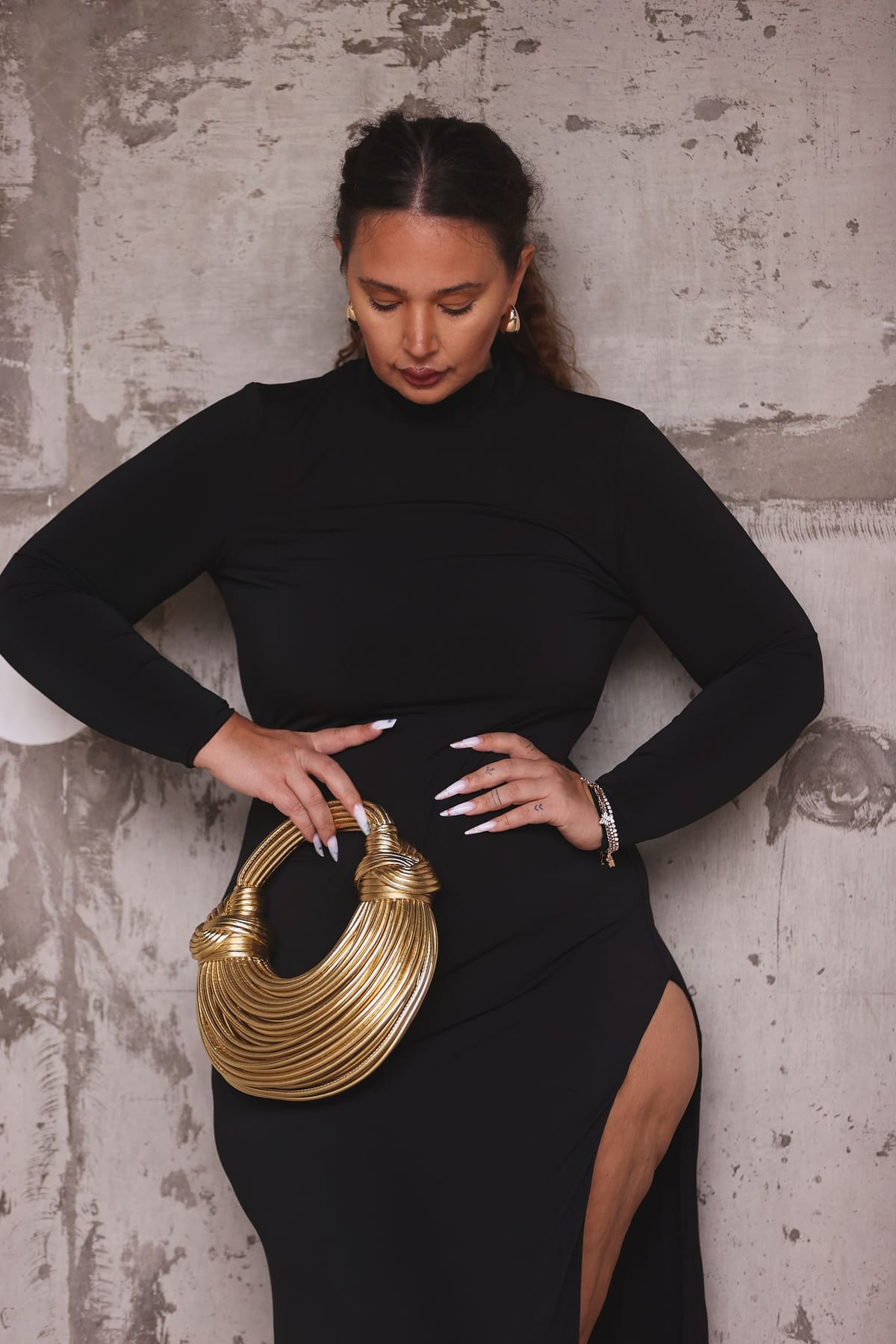 Ms Curvaceous model Oana at full length on location against a bare concrete wall in a black dress.